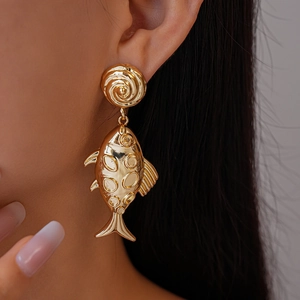 Detailed view of large gold metallic fish earrings with a vintage textured finish