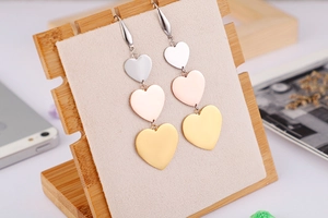 Detail view of triple heart dangle earrings in gold, silver, and rose gold finishes