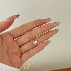 Detail of hand holding a gold heart pendant necklace with three white zircons