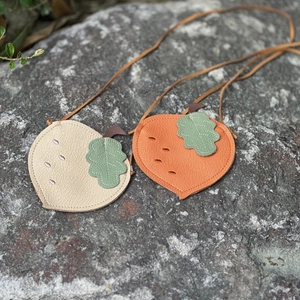 Close-up of litchi grain leather kids cross-body bags with green leaf charms on rock