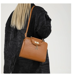 Detail of brown crocodile pattern handbag with deer pendant on a black coat model
