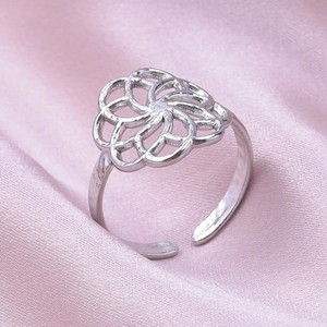Bague réglable argentée avec motif de pétales sur satin rose, vue macro détaillée