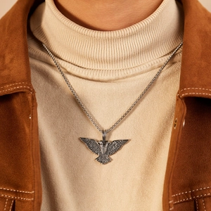 Close-up of a silver double-headed eagle pendant on a box chain worn over a sweater