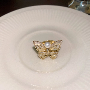 Macro detail of a gold butterfly ring featuring white mother-of-pearl and a central pearl