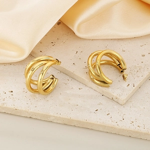 Polished gold C-shaped triple hoop earrings on beige stone and silk background