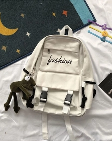 White canvas backpack with black fashion embroidery and frog charm on white sheet