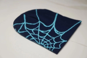 Close-up of navy knit beanie featuring a teal jacquard spider web pattern texture