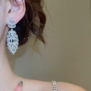 Detail of silver long drop earrings with leaves and sparkling zircons on model ear