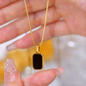 Golden titanium steel necklace with square black pendant shown in hand closeup