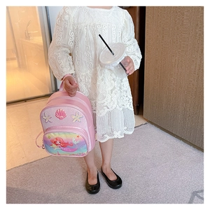 Detail of pink mermaid princess backpack held by a girl in a white lace dress