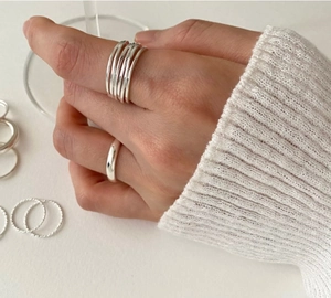 Close-up of multi-layer silver rings on hand holding a glass, minimalist jewelry style