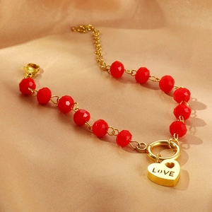 Dettaglio del bracciale con perline rosse e ciondolo a cuore dorato con scritta LOVE