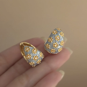 Macro detail of vintage grey enamel C-hoop earring with golden flower and small crystals