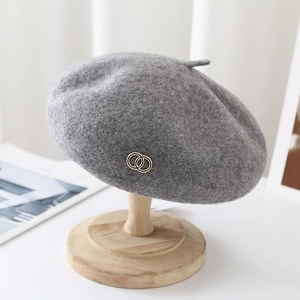 Detail of grey wool beret with golden metal rings on a wooden stand in a cozy setting