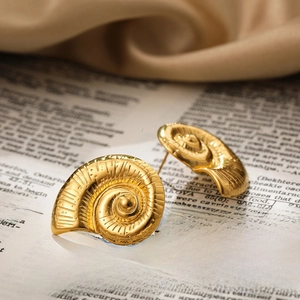 Macro detail of gold seashell earrings resting on a vintage newspaper and beige fabric