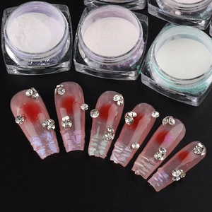 Macro view of Aurora pearl nail powder jars and translucent pink false nails with rhinestones