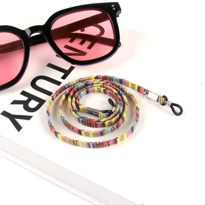 Detail of bohemian colorful woven eyewear lanyard with metal clips on a white book