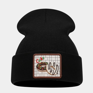 Detail of black knitted beanie showing square patch with cake and donut embroidery