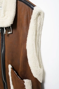 Detailed macro view of brown faux suede vest showing white sherpa lining and metal buckle