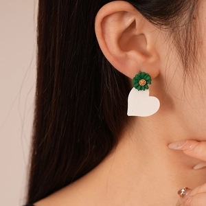 Detail of green daisy flower and white heart acrylic asymmetrical earrings on earlobe