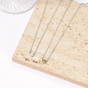Minimalist silver chain necklaces with white and green zircon heart pendants on stone