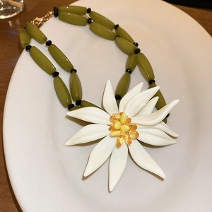 Detail of a white floral pendant necklace with yellow beads and green bamboo-style resin chain