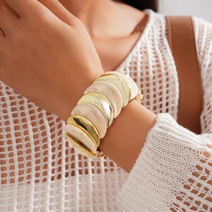 Primo piano di un ampio bracciale in resina acrilica e metallo dorato indossato da una donna