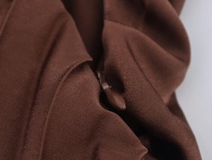 Macro shot of invisible zipper and seam detail on a dark brown pleated dress