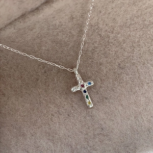 Dettaglio macro del ciondolo a croce in argento con zirconi colorati su tessuto operato