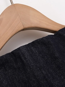 Detailaufnahme der hochwertigen dunkelblauen Denim-Stofftextur auf einem Holzbügel