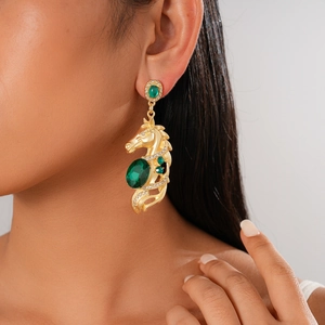 Close-up of a golden horse head earring with a large green oval gemstone and clear crystals