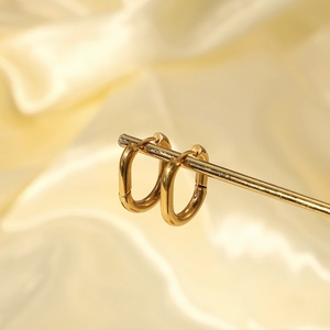 Close-up of gold U-shaped earrings on satin background, high-quality stainless steel jewelry