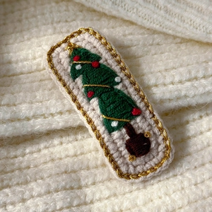 Detailed close-up of handmade embroidered Christmas tree hair clip with golden trim
