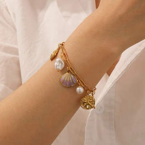 Gold ocean themed bracelet with starfish, seashell, and pearl charms on model's wrist