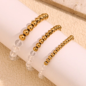 Three-piece gold beaded bracelet set with clear acrylic beads on a display stand