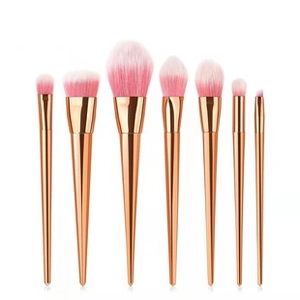 Set of seven rose gold makeup brushes with pink gradient bristles on a white background