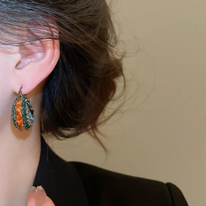 Nahaufnahme von Vintage-Creolen mit orangefarbenen und grünen Kristallen auf strukturiertem Metall