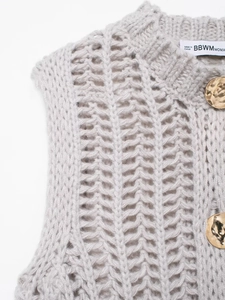 Dettaglio del gilet in maglia grigio chiaro con trama a V traforata e bottoni dorati