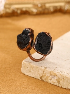 Macro view of vintage bronze double-stone ring with raw black ores on a beige stone base