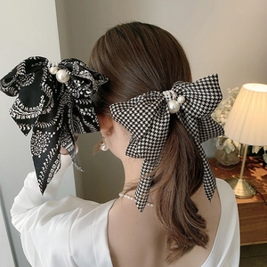 Houndstooth and paisley bow hair clips with pearl detail worn by a model in a warm setting