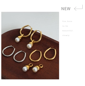 Detail of gold and silver steel hoop earrings with removable pearl charms on wood