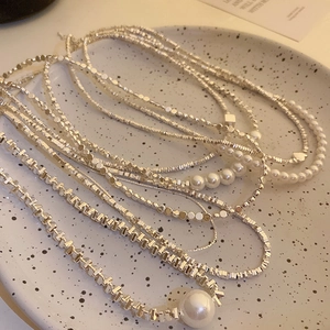 Detailed view of layered silver-toned necklaces with pearls on a ceramic tray