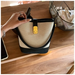 Detail of beige canvas and black leather bucket bag with gold clasp on wooden shelf