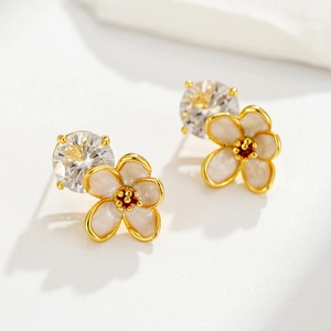 Macro shot of gold-plated flower earrings with white enamel petals and clear zircon center