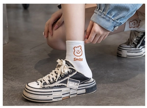 Detail of white mid-calf socks with brown bear pattern and Smile text on a model