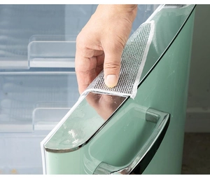 Close-up of transparent mesh protective strip being applied to a green refrigerator edge