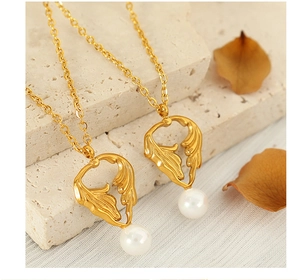 Golden leaf necklace with pearl pendant displayed on beige stone with dried leaves