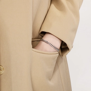 Close-up of a silver stainless steel Cuban link bracelet on a wrist with a khaki trench coat