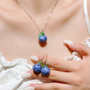 Detail view of a blue blueberry pendant necklace and matching earrings on model