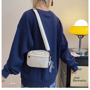 Détail du sac bandoulière en nylon blanc cassé avec étiquette FASHION et large sangle